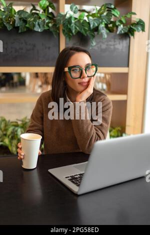 Distracted from work worried young woman sitting on desk with laptop, thinking of problems. Pensive unmotivated lady looking at monitor, feeling lack of energy, doing remote freelance tasks Stock Photo