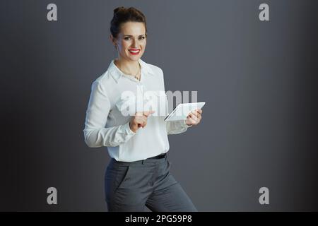 smiling modern middle aged small business owner woman in white blouse using app on tablet PC isolated on grey background. Stock Photo