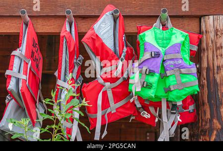 Fairbanks, Alaska, USA - July 27, 2011: brightly colored red and green lifevests hang from brown wooden beam. Stock Photo