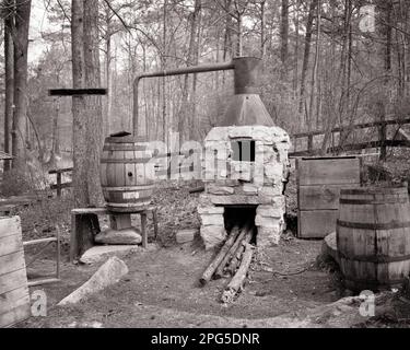1960s OLD TIME HILLBILLY MOONSHINE STILL IN WOODS STONE FIREPLACE COPPER KETTLE THAT DISTILLS INTO WOODEN BARREL - o2715 HAR001 HARS BLACK AND WHITE DISTILLATION HAR001 OLD FASHIONED Stock Photo