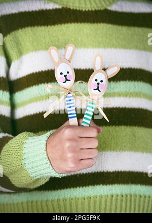 Two handmade colorful cute bunnies made from wooden spoons in child hand. Small gift or decor for Easter. Easy fun kids crafts concept. Stock Photo