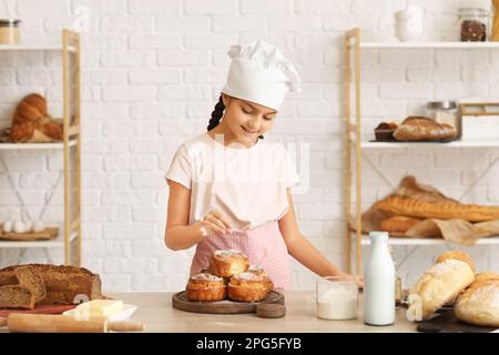 Little baker sprinkling sugar powder onto buns in kitchen Stock Photo