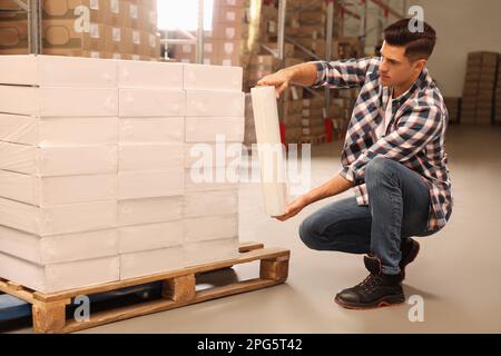 Worker wrapping boxes in stretch film at warehouse Stock Photo