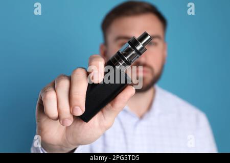 Man holding electronic cigarette against light blue background, focus on hand Stock Photo