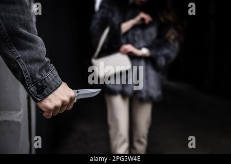 Criminal with knife hiding behind wall and waiting for victim near alley, closeup Stock Photo