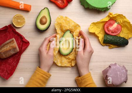 Woman packing half of fresh avocado into beeswax food wrap at wooden table, top view Stock Photo