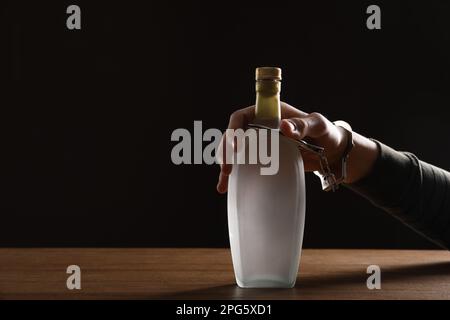 Alcohol addiction. Man handcuffed to bottle of vodka at wooden table, closeup. Space for text Stock Photo