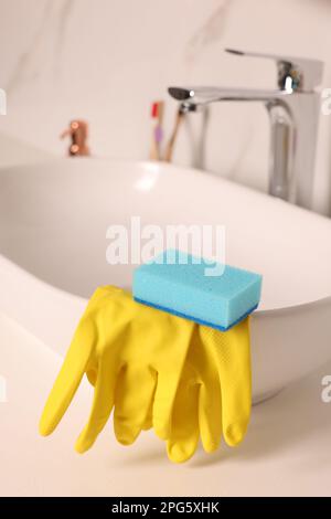 Sponge and rubber gloves on bathroom sink indoors Stock Photo