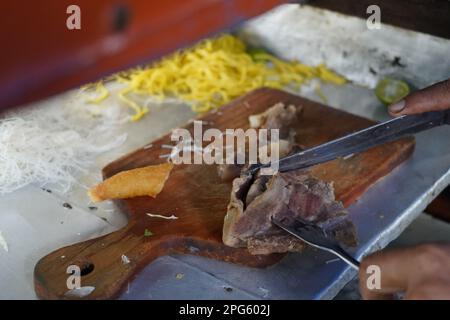 Beef brisket being chopped into bits on a wooden cutting board. with yellow noodle on the background. Preparation for beef noodle soup in Indonesia. Stock Photo