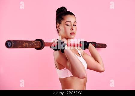 You earn a lot more when you dont give up. Studio shot of a sporty young woman exercising with a barbell against a pink background. Stock Photo