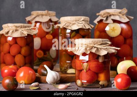 Various types of canned tomatoes with carrot, apples, horseradish, garlic and chili pepper in glass jars for long-term storage Stock Photo