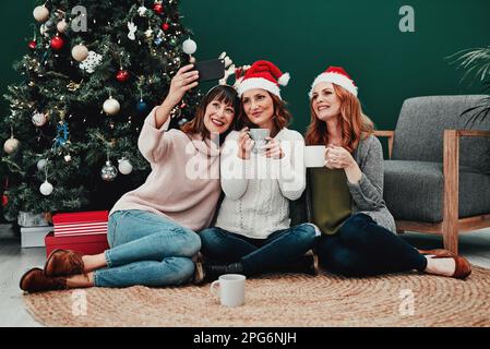 This photo is going to come out great. three attractive middle aged women taking self portraits together with a cellphone at home during Christmas Stock Photo
