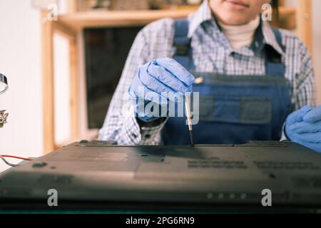 Young woman disassembling and repairing a laptop using a screwdriver works in a computer repair service center Stock Photo