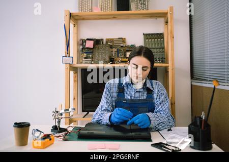 Repairs and diagnostics breakdowns of laptop in professional service center. Master repairing laptop in workshop unscrews detail with screwdriver. Stock Photo