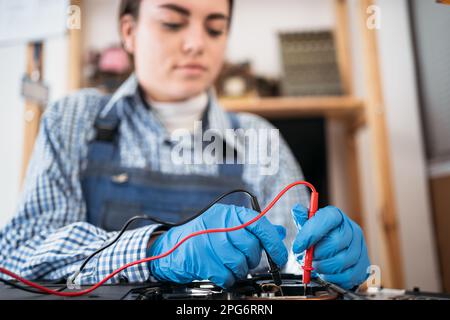 Repairman testing laptop motherboard using multimeter working in service center. Stock Photo