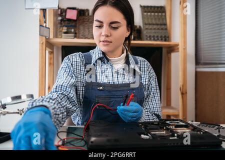 Female worker testing laptop motherboard using multimeter while working in repair computers service center. Stock Photo