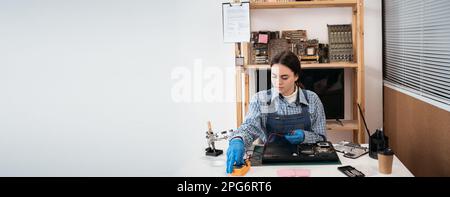 Woman repairman testing laptop motherboard using multimeter. Concentrated technician busy repairing laptop at workshop. Computer repairing concept Stock Photo