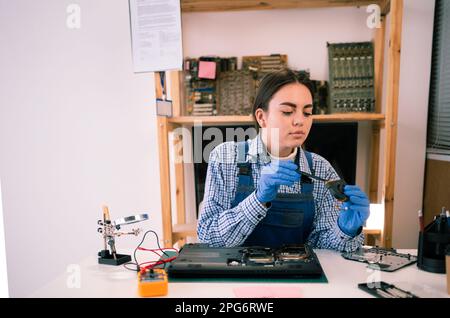 Female repairman working in technical support fixing computer laptop. Disassembling a notebook and cleaning its cooling system. Stock Photo
