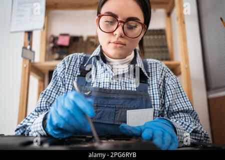 Close-up of female technician repairing laptop at desk. Engineer performing laptop maintenance. Hardware developer fixing electronic components Stock Photo