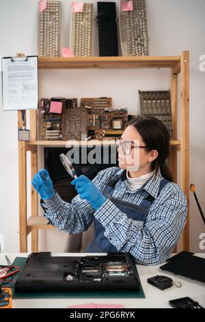 The technician holding a CPU of the laptop computer motherboard and looking through magnifying glass. computer, service, electronics, hardware Stock Photo