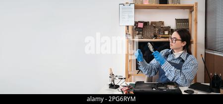 Woman looking at circuit board through magnifying glass. Engineer testing microcircuit though magnifier. Electronic renovation in repair shop Stock Photo
