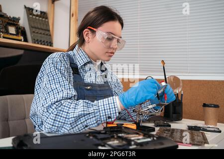 Computer service and repair concept. Woman repairing the broken laptop computer in service office. Testing laptop circuit board using multimeter. Stock Photo