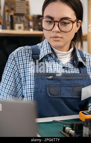 Portrait of young female technician smiling while fixing computer hardware. Stock Photo