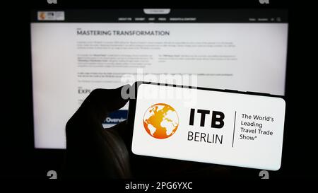 Person holding cellphone with logo of German tourism trade fair ITB Berlin on screen in front of webpage. Focus on phone display. Stock Photo