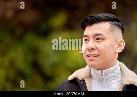 Attractive Asian man looking to the side smiling while relaxing outdoors in a park.  Stock Photo