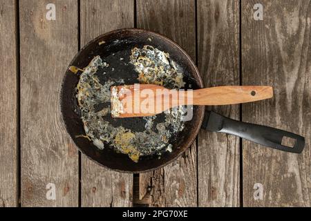 frying pan with food leftovers on a wooden table after breakfast in the kitchen at home Stock Photo