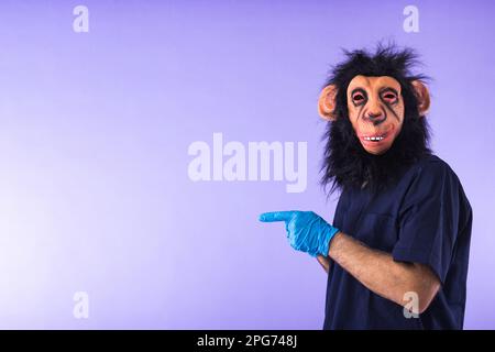 Disguised person in a monkey mask and doctor's outfit, pointing to the side with fingers, on purple background. MONKEYPOX, Pandemic, virus, epidemic, Stock Photo