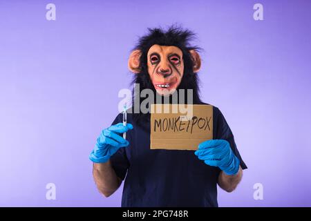 Person dressed in a monkey with a mask, with a medical nurse's suit, with a sign that reads: MONKEYPOX, and a syringe, on a purple background. Pandemi Stock Photo