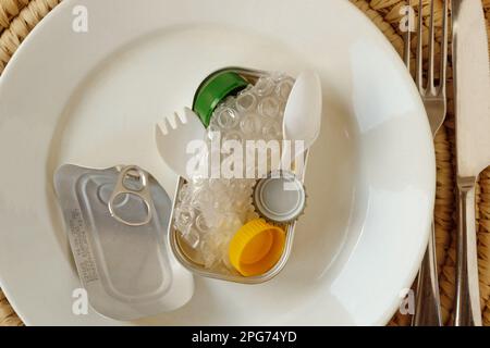 Aluminium Tuna can full of plastic trash on white plate - Concept of ecology and plastic pollution Stock Photo
