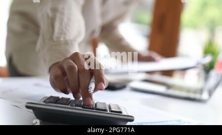 Close-up shot of Young man holding a pen and using a calculator placed in front, A man holding a pen and using a calculator. Stock Photo