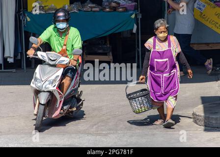 SAMUT PRAKAN, THAILAND, FEB 13 2023, A motorcyclist rides next to an elderly woman walking from the market Stock Photo