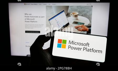 Person holding cellphone with logo of software application Microsoft Power Platform on screen in front of webpage. Focus on phone display. Stock Photo