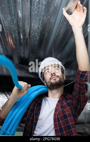 man measuring metal bar in roof space Stock Photo