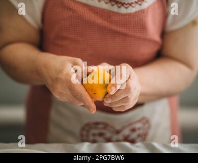Lifestyle, education. An elderly woman with down syndrome is studying in the kitchen peel the tangerine herrself Stock Photo