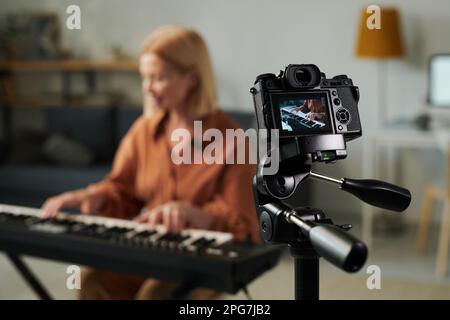 Selective focus of professional camera standing on tripod with teacher teaching musical lesson online Stock Photo