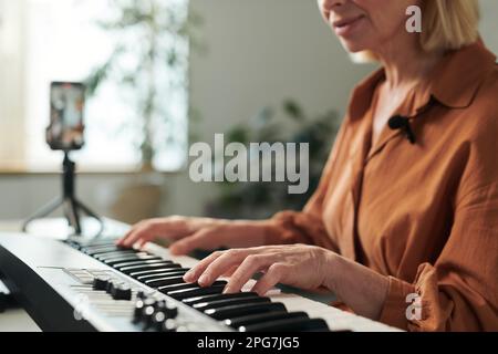 Mature teacher playing on piano online and recording her lesson on professional camera for students Stock Photo