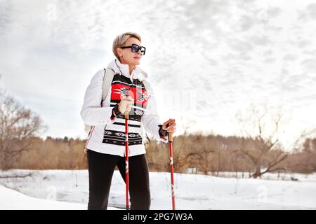 Active mature tourist woman hiking with trekking sticks in winter nature against sky Stock Photo