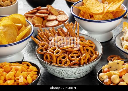 Salty snacks, party mix. An assortment of crispy appetizers in bowls on a table. Potato and tortilla chips, crackers, popcorn etc Stock Photo