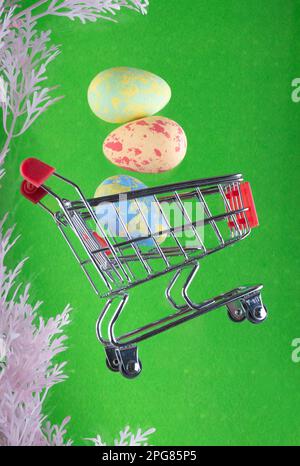 Easter sale. Shopping cart, trolley floating on green backdrop with colored eggs above. Vertical photo levitation.  Stock Photo