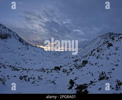 A stunning image of a snow-covered mountain landscape with a brilliant sun shining through the clouds Stock Photo