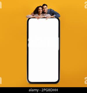 Mobile Ad. Happy Middle Eastern Couple Leaning At Big Blank Smartphone Stock Photo