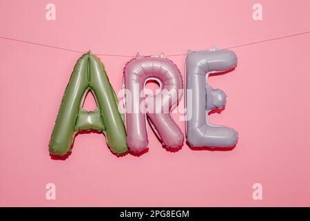 alphabet-shaped balloons of different colors forming the text are hanging from a string on a pink background with some blank space on top Stock Photo