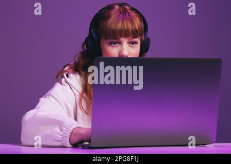 Female gamer looking focused at her laptop screen while playing an online video game in a studio. Woman using an interactive streaming service. Stock Photo