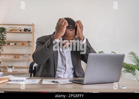 Unhappy black male worker at laptop screen shocked by gadget breakdown or operational problems. Frustrated man confused surprised by unexpected error Stock Photo