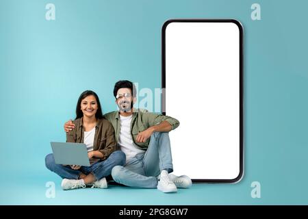 Positive mixed race couple using laptop, sitting by big phone Stock Photo