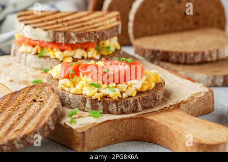 Scrambled eggs and smoked salmon on rye bread with green onions. A sandwich for breakfast. Selective focus Stock Photo